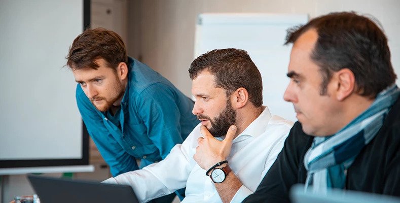 3 men discussing at as desk